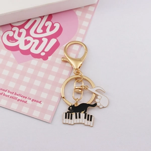 Golden cat on piano keychain with musical note paw pendant on a pink background
