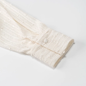Close-up of a white women's shirt cuff featuring delicate stripe texture and dot pattern