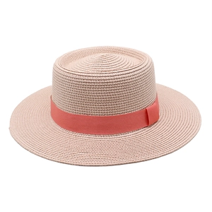 Detail of pink straw boater hat featuring a coral red ribbon trim for summer