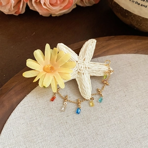 Detailed macro view of yellow daisy, raffia starfish, and gold chain tassels on hair clip