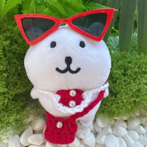 Detail of white plush pet doll wearing red cat-eye sunglasses and a knitted bowtie