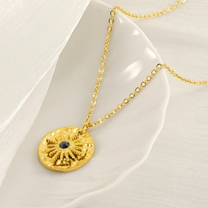 Golden sunburst coin necklace with blue sapphire center on a white seashell tray