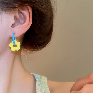 Close-up of a model wearing blue flower drop earrings with a yellow floral pendant