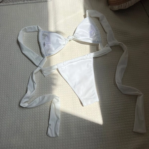 Flat lay of white satin bikini set with tie-up straps and smooth glossy fabric texture