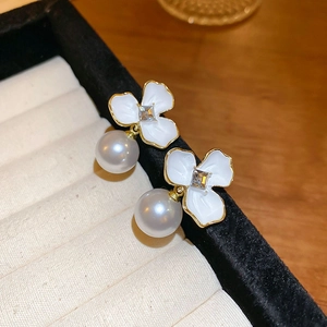 Vintage floral pearl earrings with white enamel petals and gold edging on a jewelry display