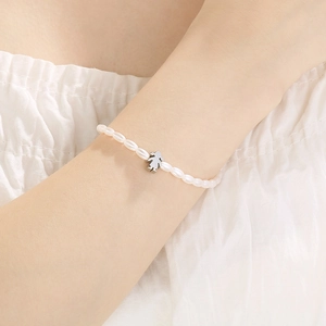 Detailed view of a white pearl bracelet with a silver girl-shaped charm on wrist