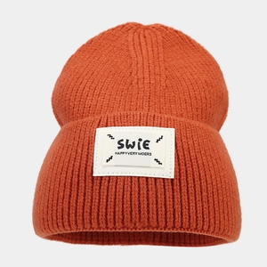 Close-up of caramel knit beanie showing soft ribbed texture and SWIE label detail