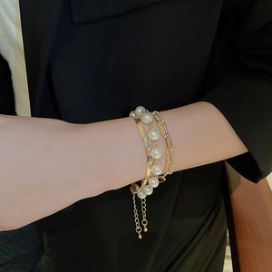 Detail of layered gold snake chain and pearl bracelet set on dark suit sleeve