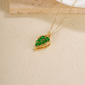 Elegant gold leaf necklace with green marquise zircon pendant on beige stone background