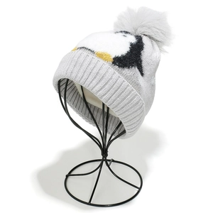 Detail of child knit hat with cute penguin pattern and a fluffy grey faux fur pompom