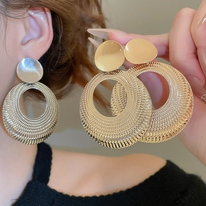 Gros plan des boucles d'oreilles rondes tressées dorées montrant la texture sur le modèle