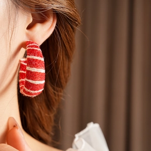 Close-up of model wearing red and white woven C-shape hoop earrings with textile texture
