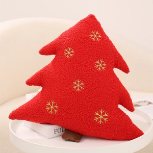 Detail of red Christmas tree plush pillow with golden snowflake embroidery on table