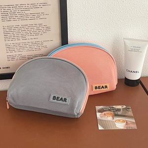 Semi-circle mesh cosmetic bag with Bear rubber label on a textured wood surface
