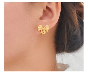 Close-up of golden bow-shaped stainless steel stud earring worn by a model
