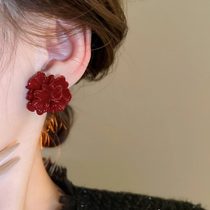 Close-up of red floral stud earring with glossy finish on model's ear in warm studio light