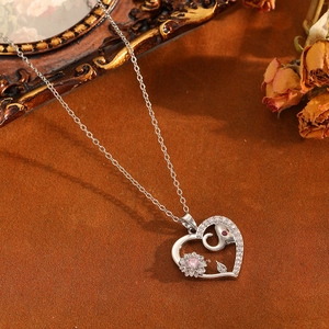 Vue macro du collier cœur argenté avec fleur en pierre rose et détail éléphant en cristal