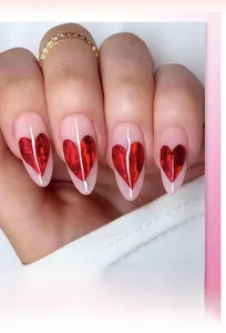 Detail of almond-shaped nude press-on nails with shiny red heart patterns and gold ring