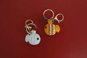 Detail of handmade crochet clownfish keychains in blue and orange with gold rings