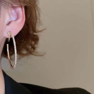 Side view detail of a model wearing large golden hoop earrings with sparkling crystals
