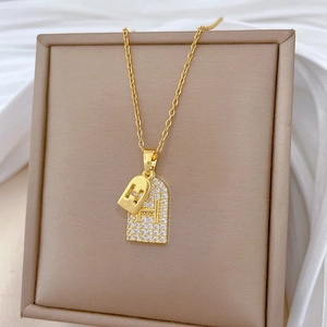 Elegant gold double pendant necklace with zircon H-letter tag and lock on silk background
