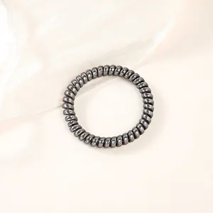 Macro detail of high-elasticity black spiral hair tie on minimalist fabric background