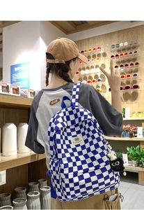Blue and white checkered backpack with a black plush charm and brand tag on back