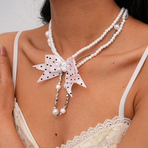 Close-up of double-layer faux pearl necklace with pink polka dot ribbon bow on a model