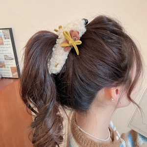 Detail showing plush cream hair claw clip with a brown bear and yellow velvet bow decoration