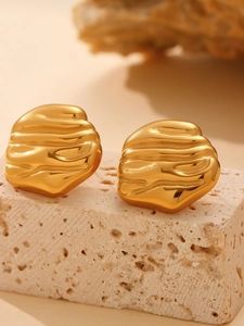 Macro detail of irregular textured warm gold earrings on beige stone background