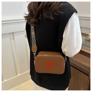 Close-up of brown camera bag with red heart print and geometric wide strap shown on model