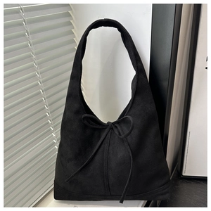 Detail of black suede tote bag featuring a decorative bow and minimalist shoulder strap