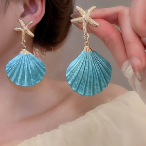 Detailed shot of gold starfish earrings with blue shell pendants on a model