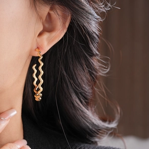 Close-up of a model wearing the large wavy gold C-shape hoop earrings with metal texture