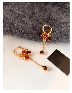 Detail of asymmetric gold tassel earrings featuring tiger eye stones and pearls