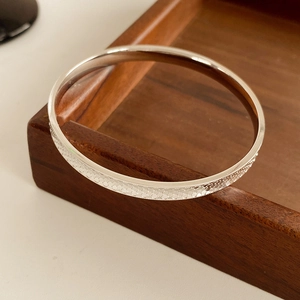 Macro view of minimalist silver round bangle with textured honeycomb pattern on dark wood