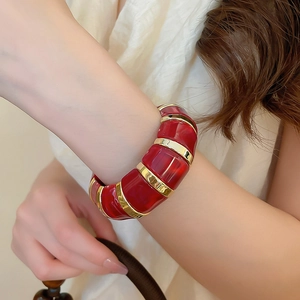 Detail shot of a wide gold metal and red resin segments bracelet on a wrist