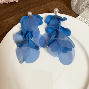 Detail of blue fabric flower earrings with faux pearls and fringe on a white plate