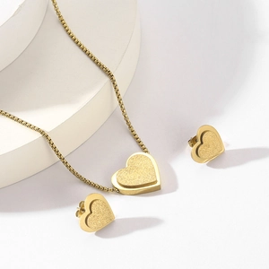 Detailed view of matte gold heart necklace and stud earrings set on a white prop
