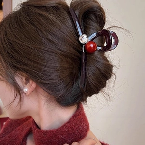 Détail de la pince à cheveux en acrylique marron avec perle rouge et strass sur modèle
