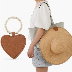 Close-up of heart-shaped leather hat clip with gold metal ring on a straw hat