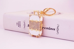 Macro detail of white rhinestone encrusted suitcase keychain with gold metal ring charm