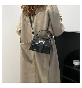 Detail of elegant black crossbody bag with a golden H-shaped clasp on a light-colored coat