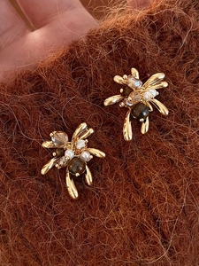 Dettaglio di orecchini a fiore con perle occhio di tigre e piccole perle su peluche marrone
