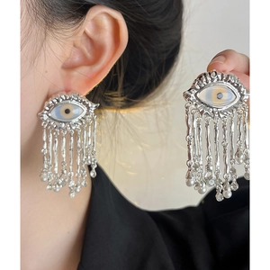 Close-up of silver evil eye earring with liquid metal texture and long fringe tassels