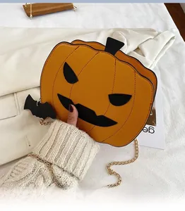 Close-up of pumpkin crossbody bag with bat charm and gold chain on white fabric