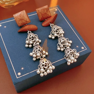 Detail of bohemian wood square earrings with silver metal bell tassels on a gift box