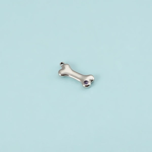 Close-up of silver dog bone pendant with purple zircon inlay on light blue background