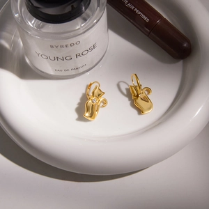 Close-up of golden cat-shaped earrings with white zircon on a white ceramic plate