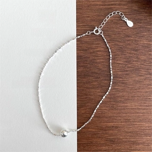 Macro detail of S925 sterling silver bead anklet with lobster clasp on minimal wood background